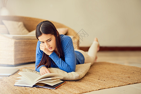 真的是沉浸在剧情中 一位年轻女子在家里的休息室地板上看书的镜头图片