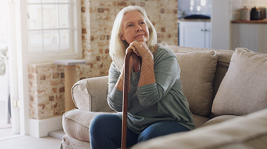 我想知道我今天能做什么 照片中一位老年妇女独自坐在家里的沙发上 手里拿着手杖 看上去若有所思背景图片