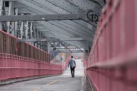 在美国纽约市布鲁克林威廉斯堡大桥的自行车道上行走的单身休闲男子图片
