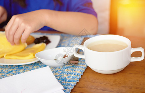 茶杯或碗汤在模糊的盘子上 吃早餐时加泡菜 果酱和手图片