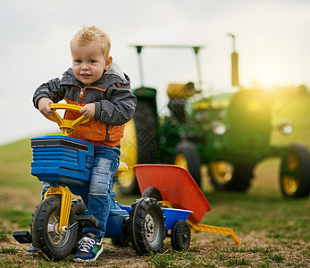 没有什么比拥有一个农场作为游乐场更好的了 一个可爱的小男孩在农场上骑玩具卡车的画像图片