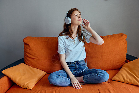 橙色沙发上的漂亮女人 用耳机技术收听音乐的歌声公寓乐趣女性音乐黑发客厅微笑快乐闲暇房间图片