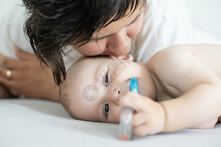 母亲和孩子在一张白色的床上 穿着尿布的妈妈和男婴在卧室里玩耍 父母和小孩在家里放松 一家人在一起玩得很开心房间玩具儿子纺织品女士图片