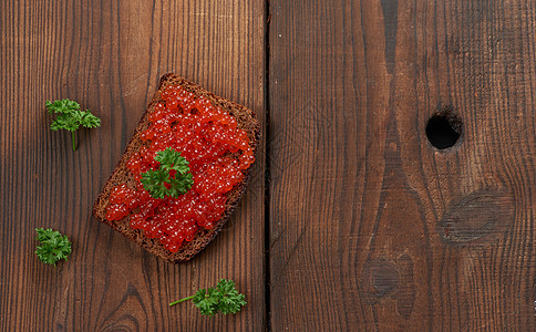 红鲑鱼子酱躺在一块黑麦面包上 棕色木桌食物海鲜小吃桌子红色奢华美味盐渍美食橙子图片
