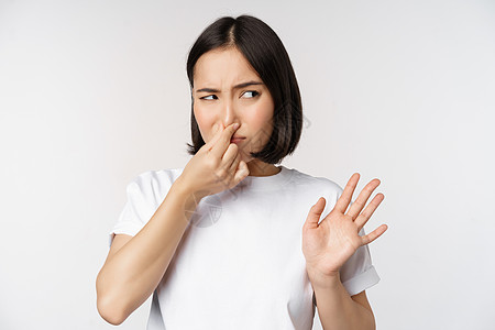 亚洲女孩看起来反感 拒绝产品与臭味不良 特写鼻子远离厌恶和不信任 站在白色背景下站立技术工作室情感学生横幅广告女性女朋友企业家成图片