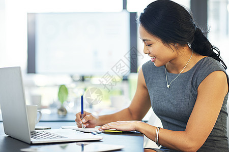 将计划纳入考虑范围并写在纸上 一位年轻女商务人士在现代办公室的笔记本电脑上工作时写笔记的裁剪镜头图片