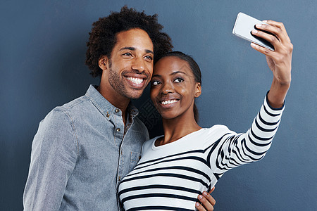 新的个人资料图片 拍摄一对快乐的年轻夫妇用灰色背景的手机给自己拍照图片