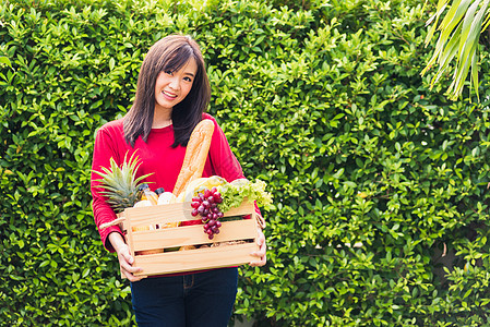 站立的女农民在木箱中持有全新鲜食品原蔬菜水果图片