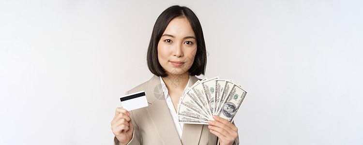 近距离接近的亚洲女商务人士 办公室女士展示信用卡和美元 站在西装白背景上站着商务人士售货员商业女孩管理人员工作室信用技术冒充图片