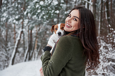 女孩头转向镜头 在冬季公园与她的狗一起散步时笑着的黑发美女玩得开心图片
