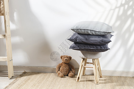 泰迪熊靠在一张小儿童凳旁边的墙上 上面放着三个灰色的枕头 梯子靠在墙上 复制空间楼梯玩具熊地毯织物柳条玩具白墙配件贮存公寓图片