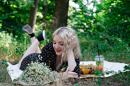 迷人的金发年轻女子在公园里野餐 吃着美味的小点心 柠檬水 水果和羊角面包 暑假 休息 放松 享受自由小吃女性季节闲暇休闲毯子食物图片