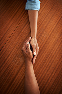 两只无法辨认的手举起双手 躺在木制桌子上 高角度拍到两只手紧紧握着对方图片