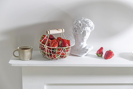 白金属篮子 有木制手柄 新鲜草莓 压实的陶瓷茶杯 石膏阿波罗头在米色桌子上浆果农业叶子厨具用具杯子食物场地雕塑维生素图片