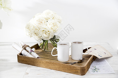一束白玫瑰花束 放在一个托盘上的玻璃花瓶里 有两杯咖啡 一瓶茶和一壶牛奶图片