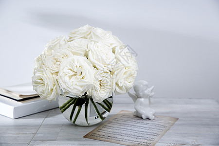 一束白玫瑰花束 放在圆杯玻璃花瓶中 桌子上有一杯茶和一本书 复制空间背景图片