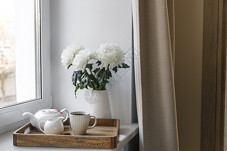 三个白菊花瓶装在七十年代式的排风花瓶里 木质餐具加水壶 奶罐和窗台上的茶杯 早饭反射茶壶家具杯子咖啡房间风格房子植物托盘图片