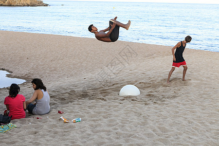 有个年轻人在沙滩上做杂技表演 跳起来了图片