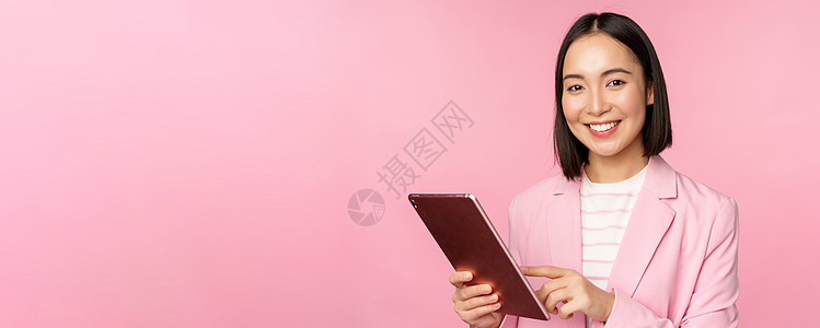 年轻亚洲公司女性的肖像 身着数字平板电脑 穿西装 微笑和看起来专业 以粉红背景作姿势的办公室女职员商业广告黑发学生人士工作室大学图片
