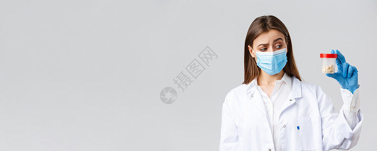 Covid19 预防病毒 医护人员和检疫概念 穿着磨砂膏和医用口罩的不确定 好奇的医生对装有药丸的容器看起来既好奇又不确定护士科图片