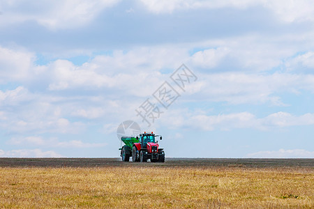 绿色拖车中的红色拖拉机正在向田间运送肥料 用于颗粒施肥的吊具拖车图片