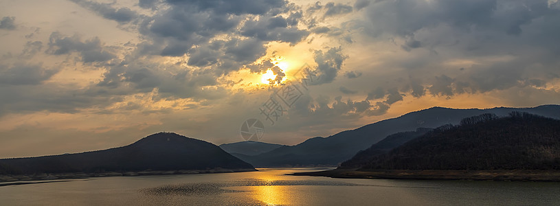 山丘之间湖的全景 有太阳反照光;图片