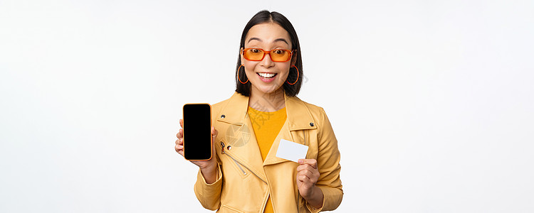 在线购物和人们的观念 站在白色背景上展示手机屏幕和信用卡 智能手机应用程序的时尚亚洲女性电话黑发广告商业技术学生微笑办公室卡片促图片