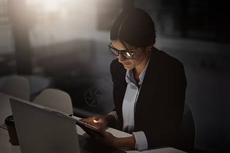 熬夜 继续工作 一位年轻女商务人士在深夜在现代办公室使用数字平板电脑和笔记本电脑的镜头图片