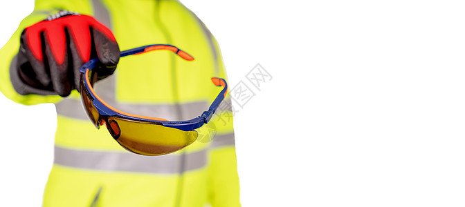 一名身穿亮黄色 hi-viz 外套和红色安全手套的建筑工人为观众提供有色安全眼镜 以保护在白色背景下隔离的眼睛 安全施工现场横幅图片