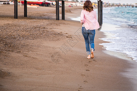 身穿牛仔裤在沙沙沙上遮光日落时跑的女子运动赛跑者活动慢跑者成人旅行日出训练天空跑步图片