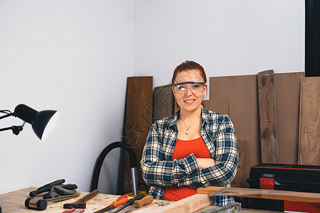 一位年轻的红头发女木匠在小型木工车间的肖像 看看摄像机 看镜头图片