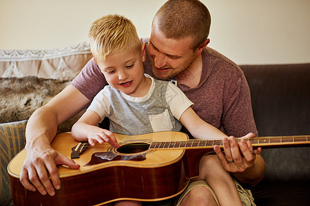 是时候和爸爸一起上另一堂吉他课了 一位父亲和他的小儿子在家里一起弹吉他的镜头图片