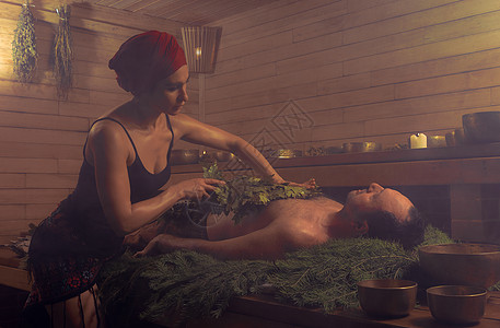 一名妇女在扫帚的帮助下为一名男子举行沐浴仪式 一个人躺在云杉树枝上疗法享受两个人男人成人治疗蒸汽女士声音女性图片