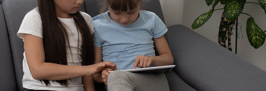 两名笑着的女孩躺在沙发上并使用平板电脑的近镜头肖像乐趣孩子们教育游戏幸福微笑技术房间享受童年图片