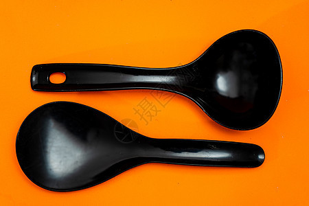 一套厨房勺子和黑塑料弹片 以橙色背景隔绝厨房用具项目工作室家庭漏勺烹饪餐具器具工具美食炊具图片