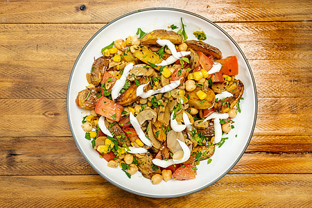 木桌上一个孤立的碗里放着美味的土豆 鹰嘴豆 番茄和蘑菇沙拉 配欧芹和蒜泥蛋黄酱 健康 自制的纯素食品图片