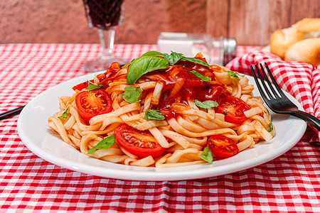 在红色方格桌布上的白盘上 可以看到意大利面配美味的自制番茄酱和自制罗勒叶 天然和自制食品的概念图片
