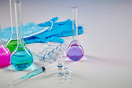 4个装有多种色化学试剂的医疗瓶 7个模型胶囊 注射器 蓝色一次性手套和白面罩被隔离在白色上图片
