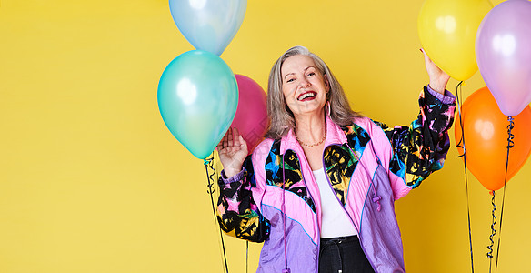 一位快乐而时髦的年长女人的肖像 在黄色背景下冒着气球 装饰着气球图片