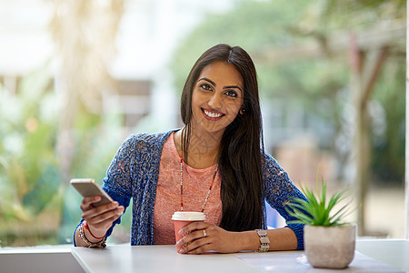 我来这里是为了无线网络 但咖啡也不错 一个年轻漂亮的女人在咖啡店里喝咖啡时使用手机的画像图片