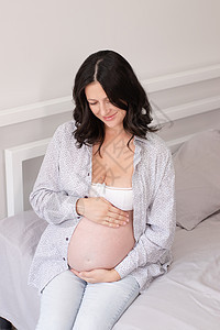 穿着床上衬衫的有魅力的孕妇 幸福怀孕治疗卧室母亲母性父母腹部女性肚子黑发孩子图片