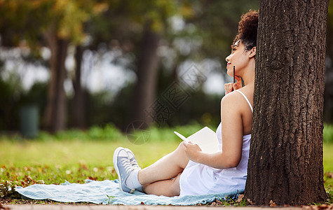 想着她的下一篇日记 一位迷人的年轻女子坐在公园里写日记的后视镜头图片