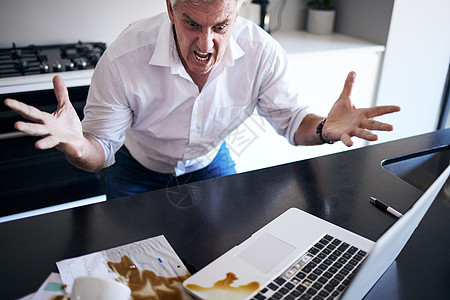 到底发生了什么 一个成熟男人在家里厨房里把咖啡洒在他的文书工作和笔记本电脑上后感到生气的照片图片