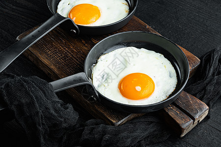 煎鸡蛋 樱桃番茄和早餐面包 在黑木制桌底的铁煎锅中图片