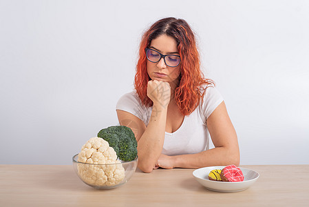 白种女人更喜欢健康的食物 红发女孩在西兰花和甜甜圈之间选择白种背景食欲蔬菜糖果重量欲望女性活力薯条脂肪保健图片