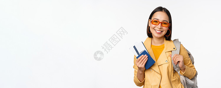 快乐的亚洲女孩去度假 拿着护照和机票 肩上背着背包 站在白色背景上出国旅行的年轻女游客广告情绪成人办公室微笑黑发女士太阳镜门票大图片