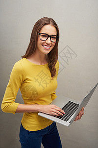 与世界相连 一个有魅力的年轻女子以灰色背景冒充笔记本电脑的工作室肖像图片