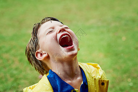 一个快乐的小男孩独自站着 张开嘴在雨天外面淋雨时大开眼界 被射中了 (笑声)图片