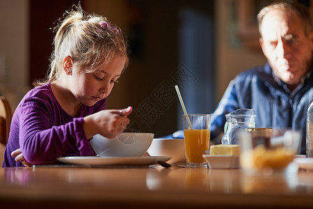 外公照看着早餐时间 一个年轻女孩在桌边吃麦片时被割伤的镜头和她的祖父一起拍到的背景图片