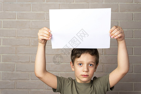 一名严重的5岁的欧洲男孩头顶上挂着一张空的海报教育白色空白广告牌推介会情绪化灰色框架小样学生图片